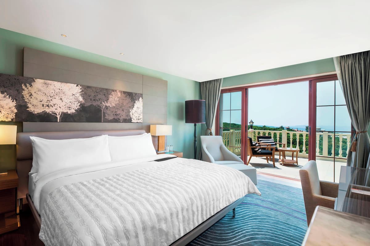 Habitación de hotel con una cama grande, vistas al exterior, un balcón con asientos y un cuadro en la pared.
