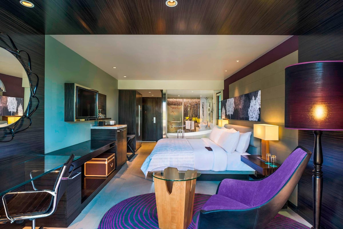 Una habitación de hotel moderna con una cama grande, un escritorio, una silla y una lámpara.