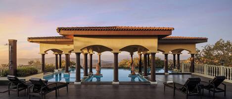 Un área de piscina al aire libre con columnas, sillones de descanso y vistas a la montaña.