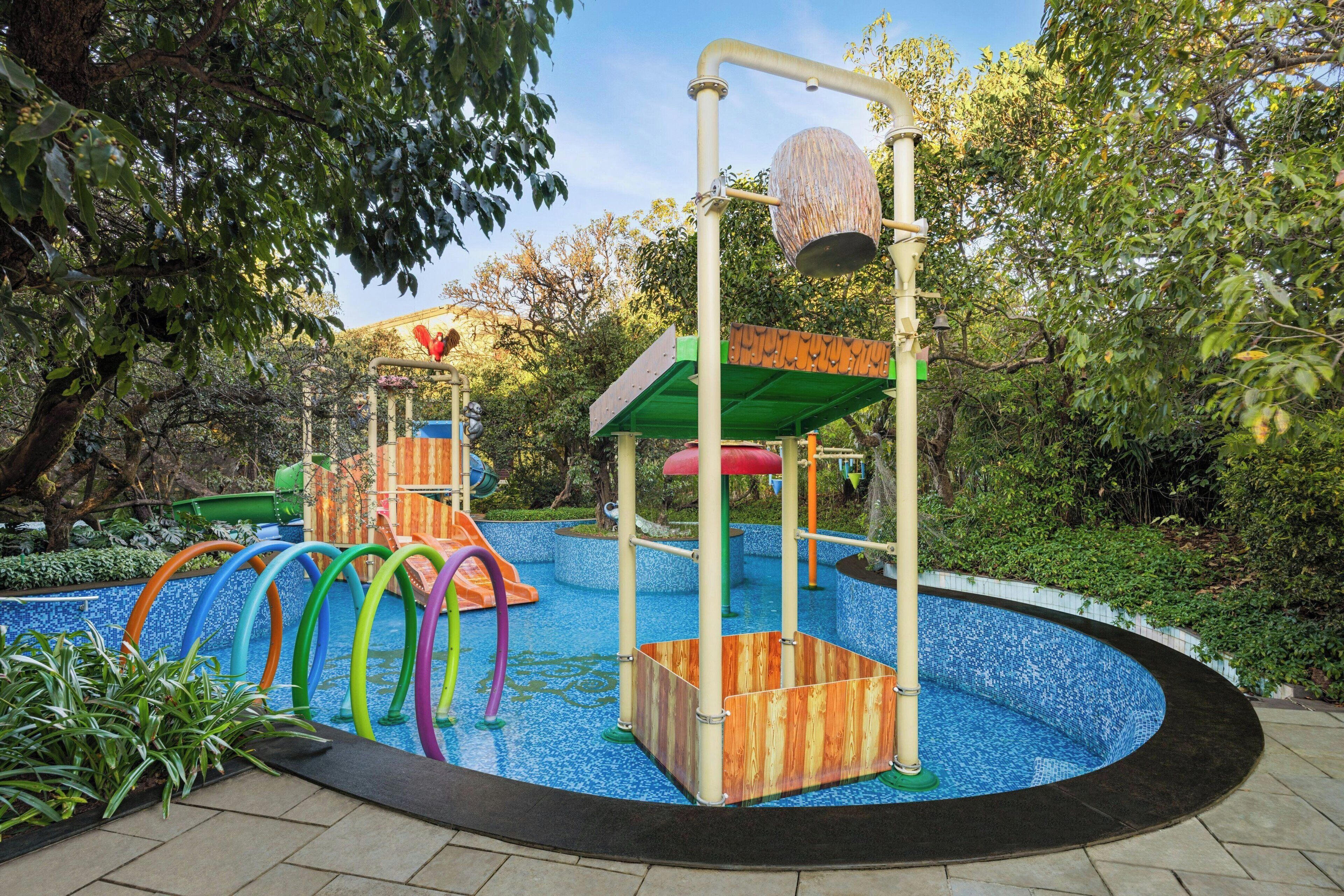 A playground with a circular blue pool, colorful slides, and a wooden climbing structure.