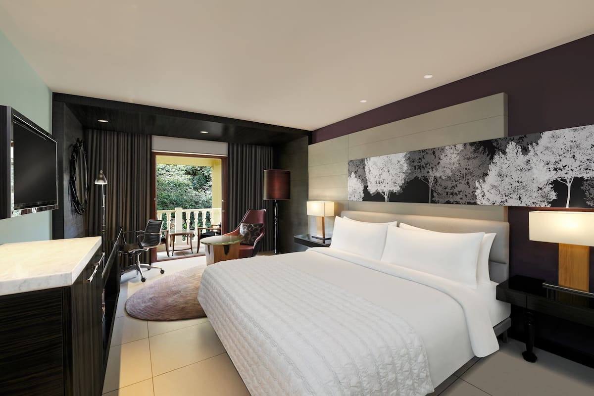 Una habitación de hotel moderna con una cama grande, un escritorio, una silla, un televisor y vistas al exterior.