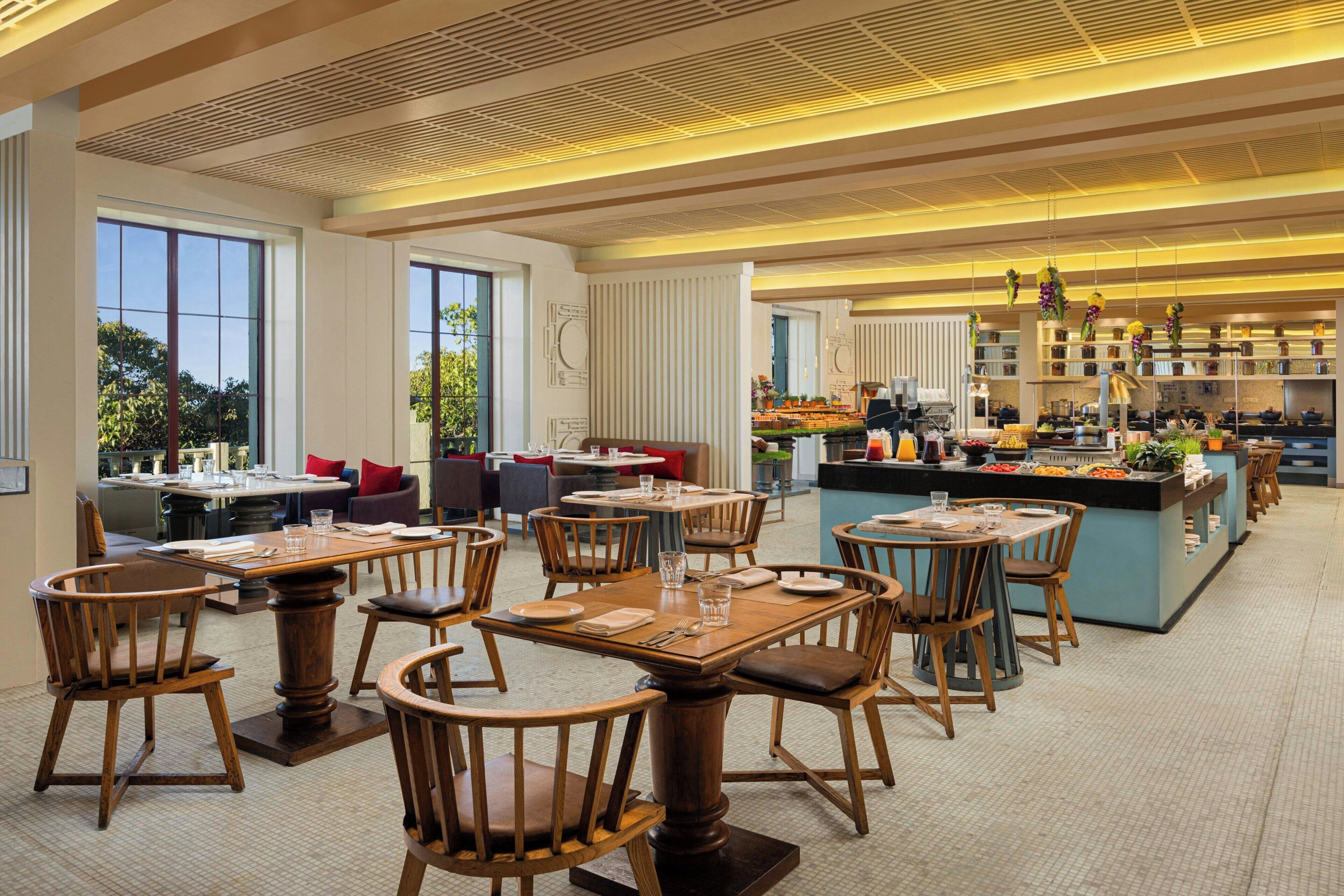 A spacious restaurant with wooden tables and chairs, a central island with a bar, and large windows offering views of the outdoors.