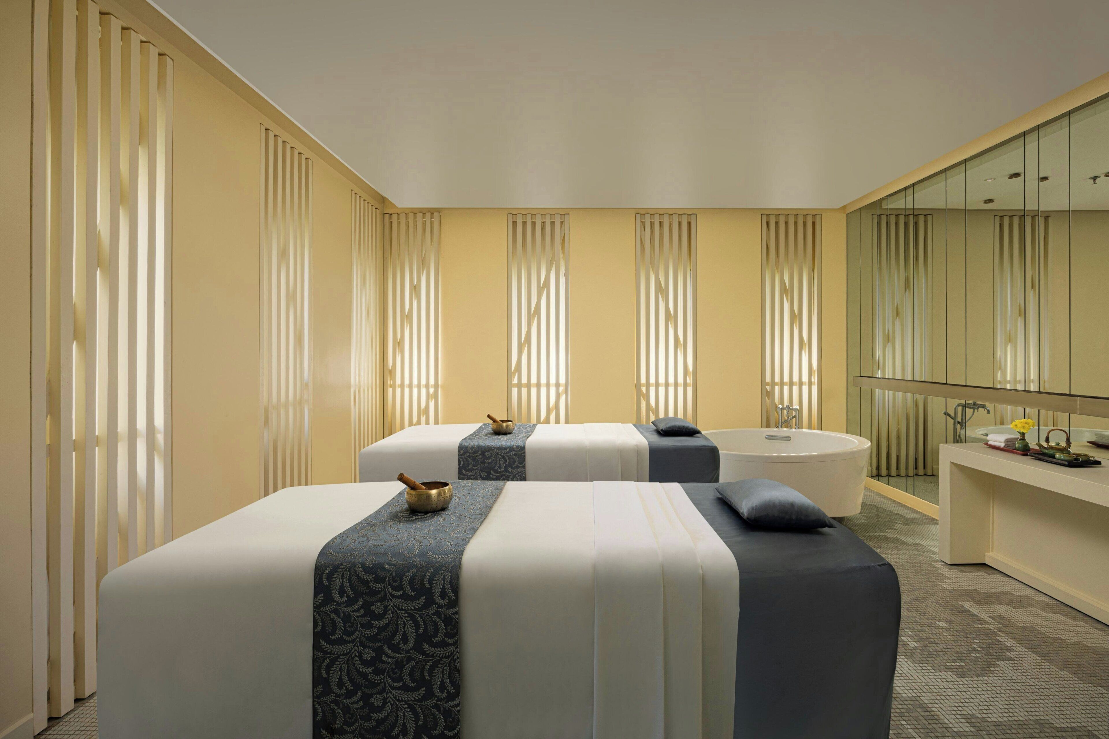 A hotel room with two beds, a bathtub, a vanity with a mirror, and a large window with curtains.