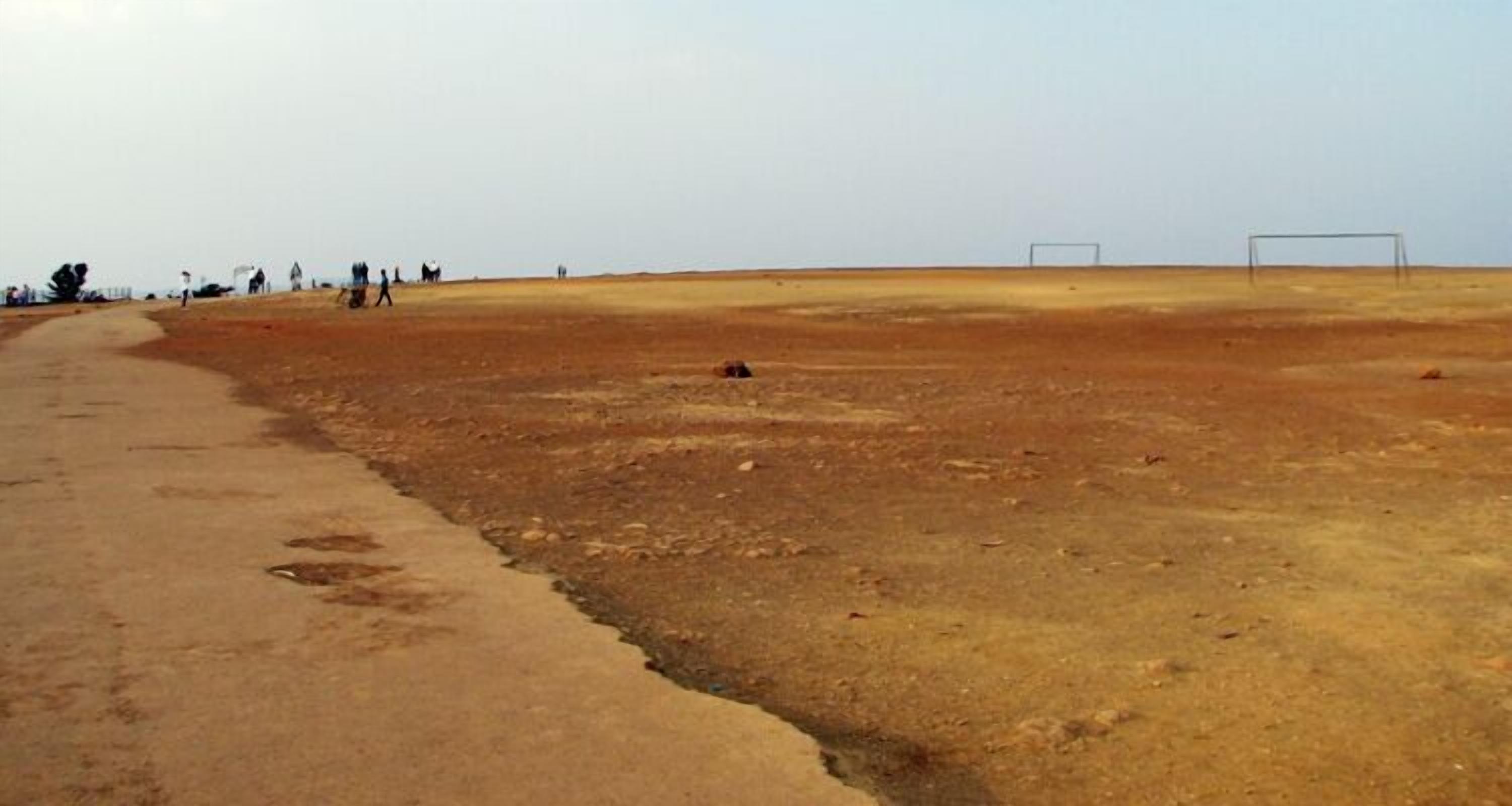 A barren landscape with a dirt path leading to a flat area with two goalposts.