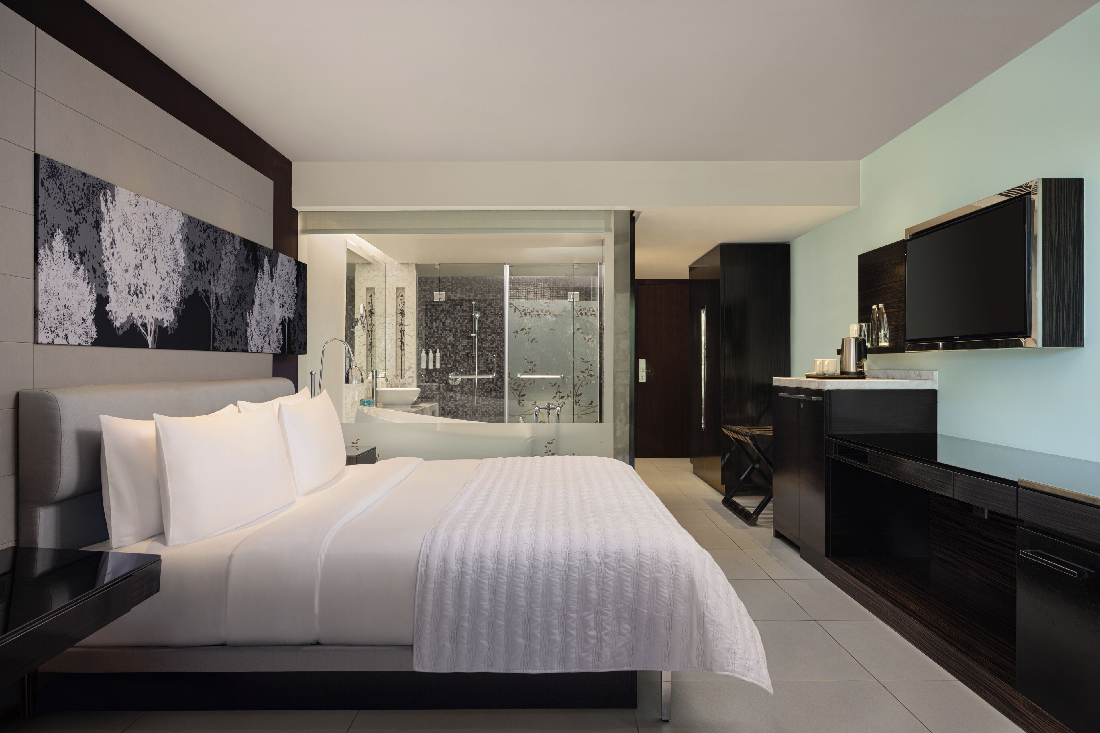 A modern hotel room with a large bed, a flat-screen TV, a bathroom with a glass shower, and a view of the city.