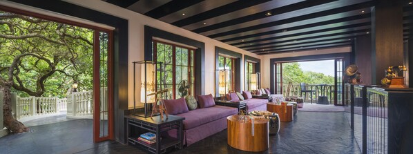 Amplia sala de estar con un sofá púrpura, una mesa de centro de madera y un ventanal con vistas a árboles.