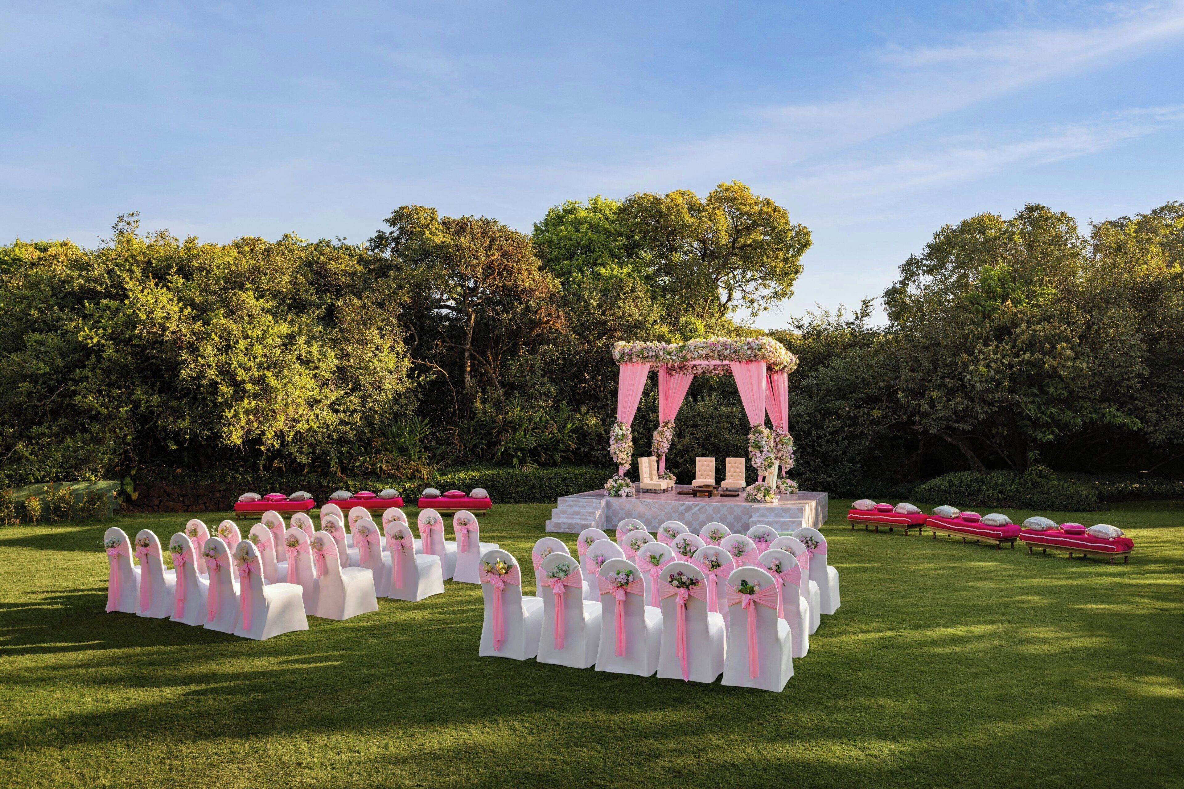 An outdoor wedding setup with rows of white chairs and a stage with pink drapery.