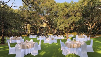 An outdoor dining area with round tables and white chairs, surrounded by trees.