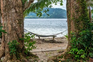 A hammock between two trees overlooking a beach with a calm sea and distant hills. - Tiliva Resort (Kadavu Island)