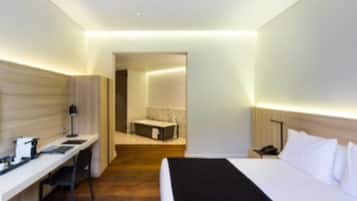 A modern hotel room with a bed, desk, and a small sitting area.
