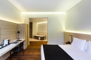 Moderni hotellihuone, jossa on sänky, työpöytä ja pieni oleskelualue.