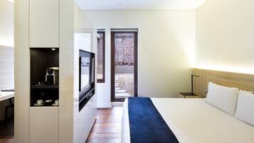 A modern hotel room with a bed, a TV, a desk with a coffee machine, and a view of a brick wall outside.