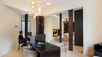 A modern living room with a dark wooden desk, clear chairs, a fireplace, and a chandelier.