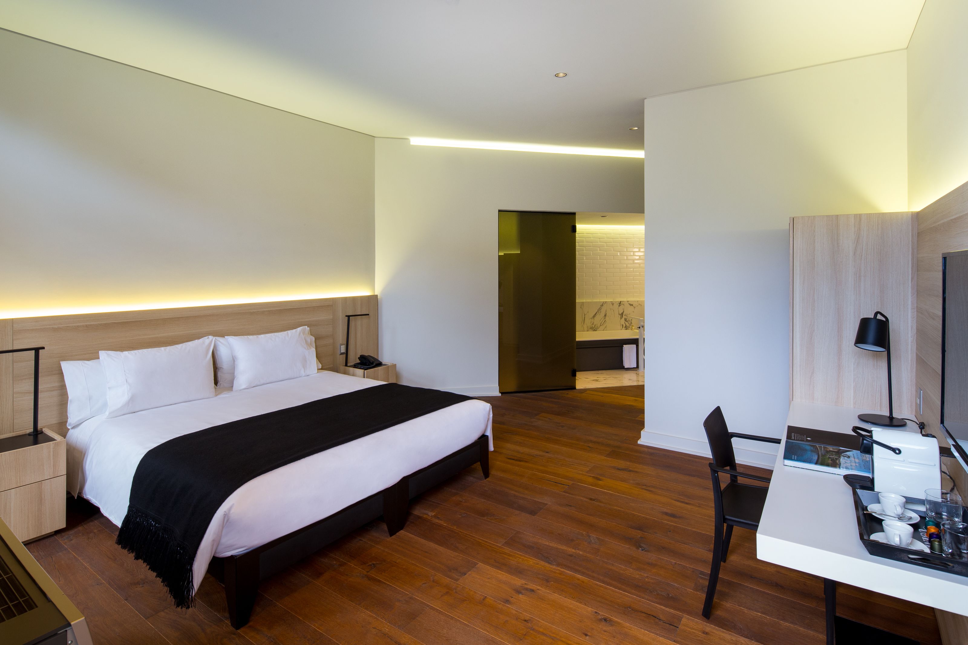 A modern hotel room with a large bed, a desk with a chair, and a television.