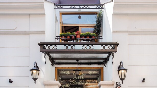 Ein Gebäude mit Balkon, einer Tür mit Schild und zwei Tischen mit Stühlen.