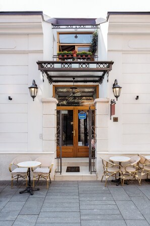 A building with a balcony, a door with a sign, and two tables with chairs.