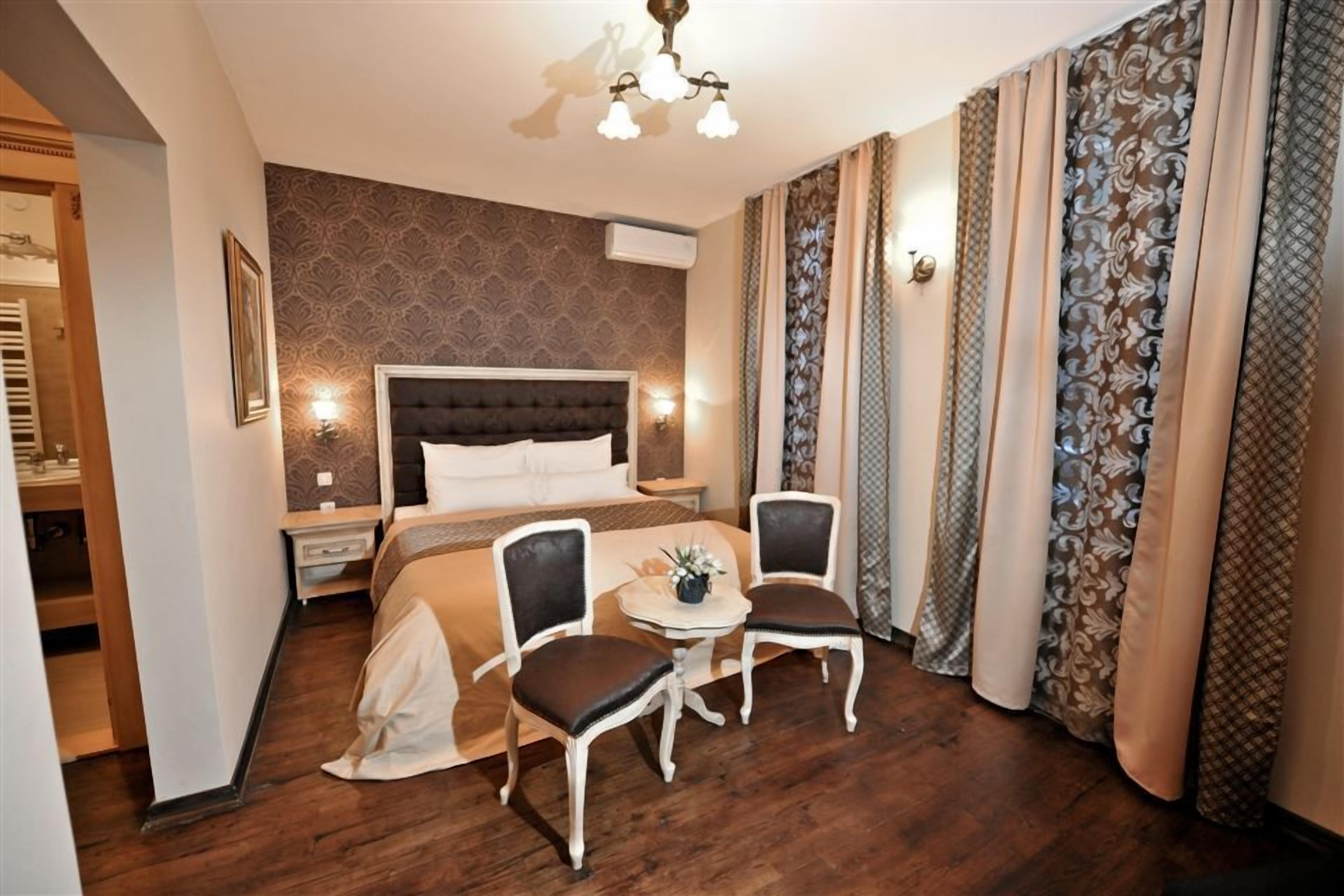 A hotel room with a large bed, two chairs, a small table, and a chandelier.
