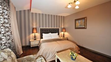 A hotel room with a bed, two bedside tables with lamps, a small table with a vase of flowers, a chair, and a painting on the wall.
