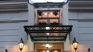 Ein Gebäude mit weißer Fassade, einem schwarzen schmiedeeisernen Tor und zwei Wandleuchtern.