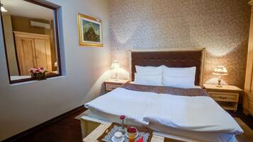 A neatly made bed with white linens, a tray with a cup, a rose, and fruit on a wooden nightstand.