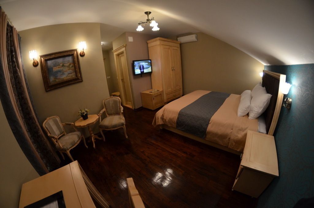 A hotel room with a bed, a television, a small table with chairs, and a wardrobe.