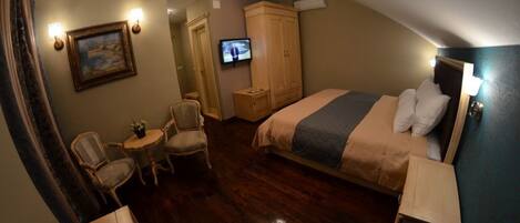 A hotel room with a bed, a television, a small table with chairs, and a wardrobe.