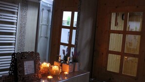 Ein Badezimmer mit Holztür, einem Fenster mit Jalousien, einem Handtuchhalter und einer kleinen Ablage mit Kerzen und einem gerahmten Bild.