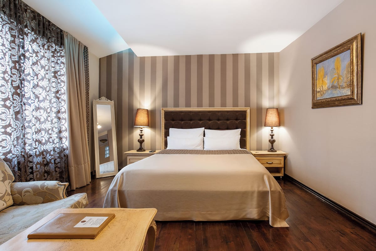 A hotel room with a large bed, two bedside tables with lamps, a sofa, and a painting on the wall.