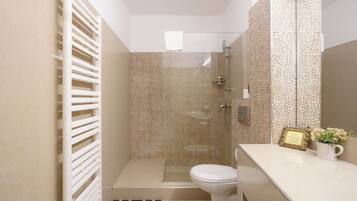 A compact bathroom with a shower, toilet, and a vanity with a mirror.