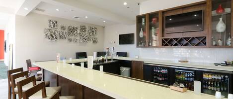 A modern bar area with a long counter, bar stools, and a wine cooler stocked with bottles.