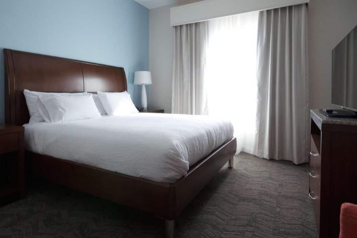 A hotel room with a bed, a TV, a lamp, and a window with curtains.