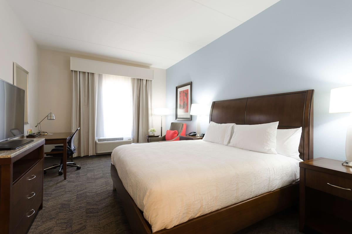 A hotel room with a large bed, a desk with a computer, a chair, and a window with curtains.