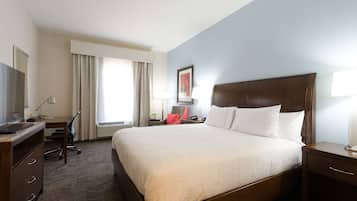 Habitación de hotel con una cama grande, un escritorio con computadora, una silla y un ventanal con cortinas.