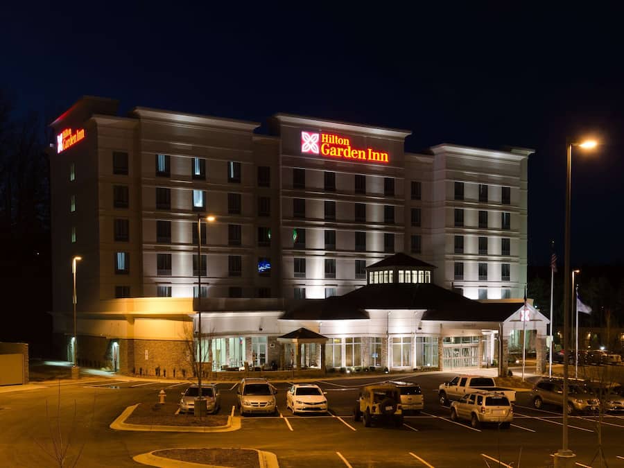 A multi-story hotel with a prominent Hilton Garden Inn sign, a covered entrance, and a parking lot with several cars.