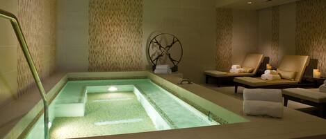 A spa area with a rectangular hot tub, lounge chairs, and a decorative wall piece.