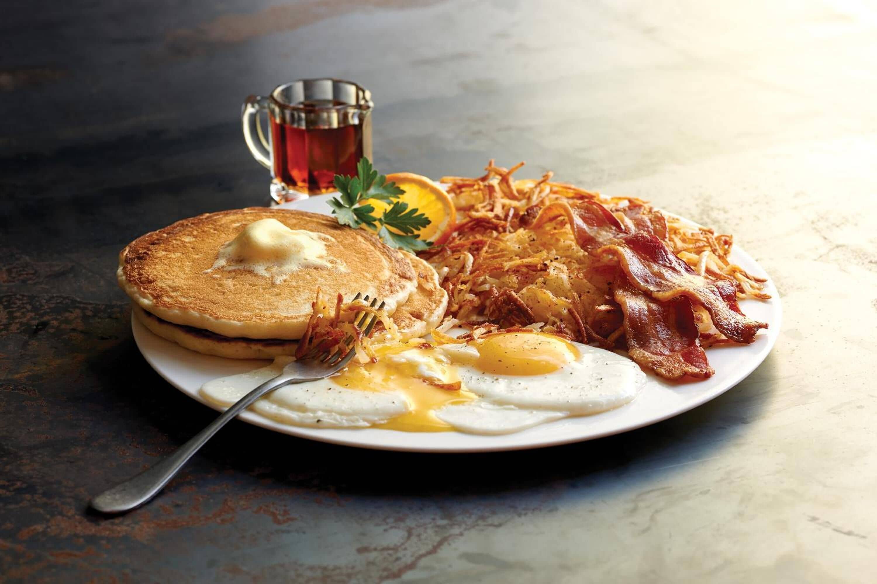 A breakfast plate with pancakes, eggs, bacon, hash browns, and a mug of coffee.