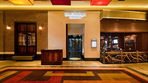 The entrance to Vic & Anthony's Steakhouse with a brick facade, a wooden bench, and a bar area with a counter and seating. - Golden Nugget Lake Charles (Lake Charles)