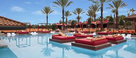 A pool area with lounge chairs and red cushioned seating, surrounded by palm trees.
