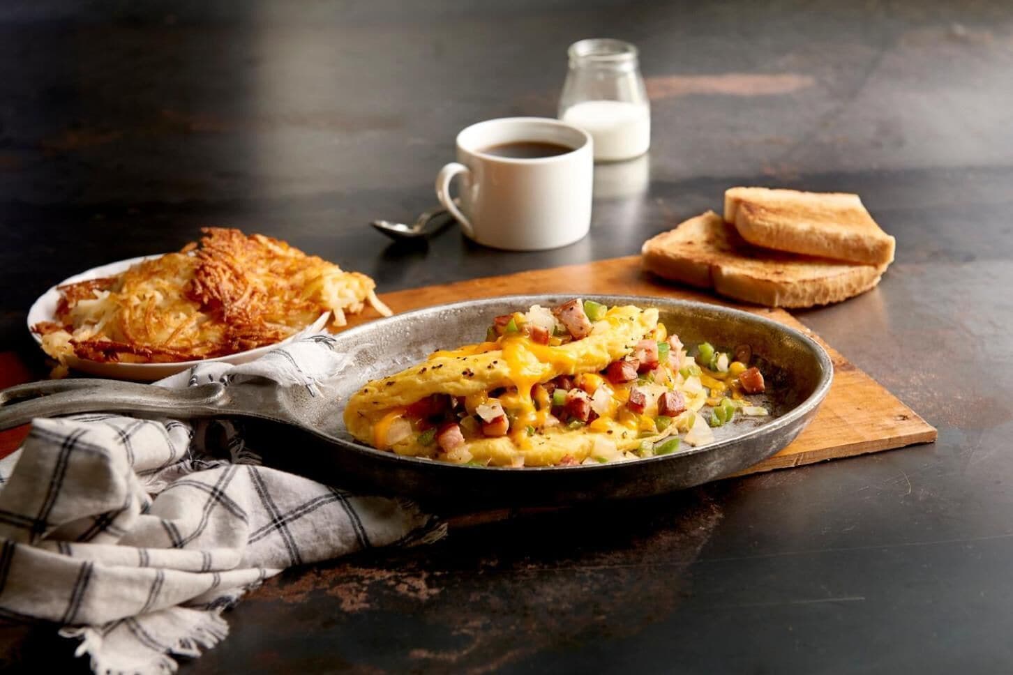 A breakfast plate with scrambled eggs, ham, and vegetables, accompanied by toast and a cup of coffee on a dark table.