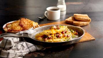 A breakfast plate with scrambled eggs, ham, and vegetables, accompanied by toast and a cup of coffee on a dark table.