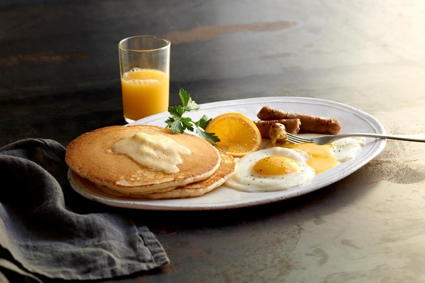 A plate with pancakes, eggs, sausages, and a glass of orange juice.