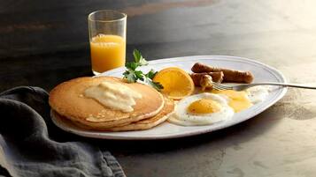 A plate with pancakes, eggs, sausages, and a glass of orange juice.