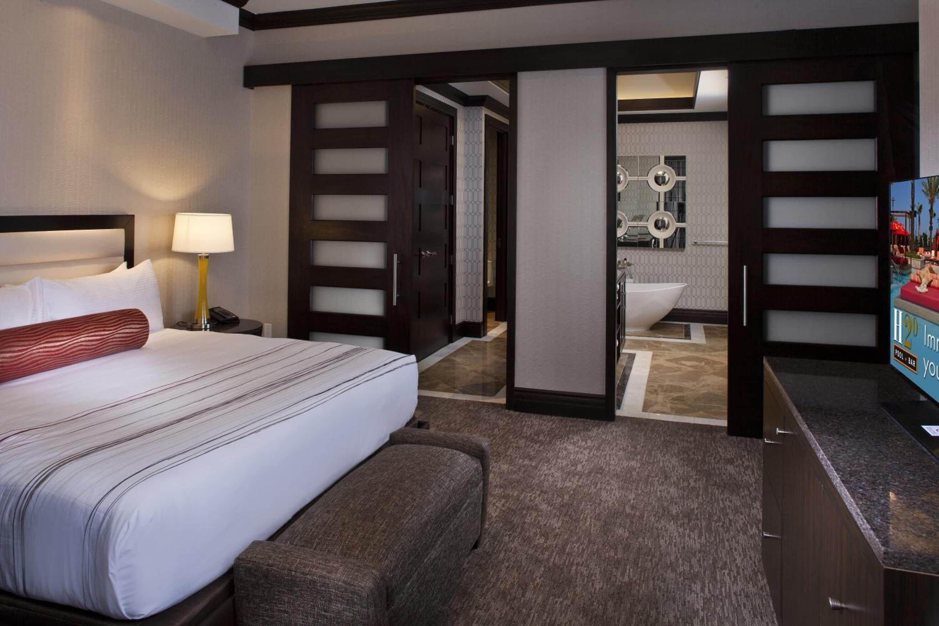 A hotel room with a bed, bedside table, lamp, and a TV.