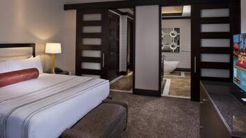 A hotel room with a bed, bedside table, lamp, and a TV.
