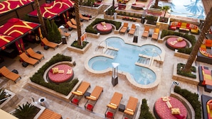 Un área de piscina con múltiples sillas de descanso y zonas de estar, rodeada de palmeras y jardines bien cuidados.