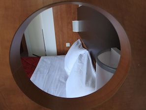 A circular mirror reflecting a hotel room with a bed, pillows, and a bedside table. - Première Classe Conflans-Sainte-Honorine (Conflans-Sainte-Honorine)