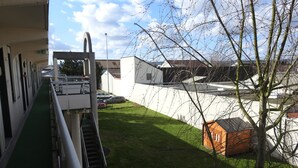 Un edificio con una rampa verde que conduce a una escalera, un estacionamiento con coches y una pequeña estructura naranja en el jardín.