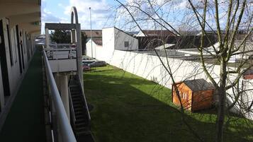 Un bâtiment doté d’une rampe verte menant à un escalier, d’un espace de stationnement avec des voitures et d’une petite structure orange dans la cour.
