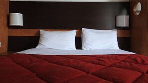 Habitación de hotel con una cama, dos almohadas blancas, una colcha acolchada roja y dos lámparas de pared.