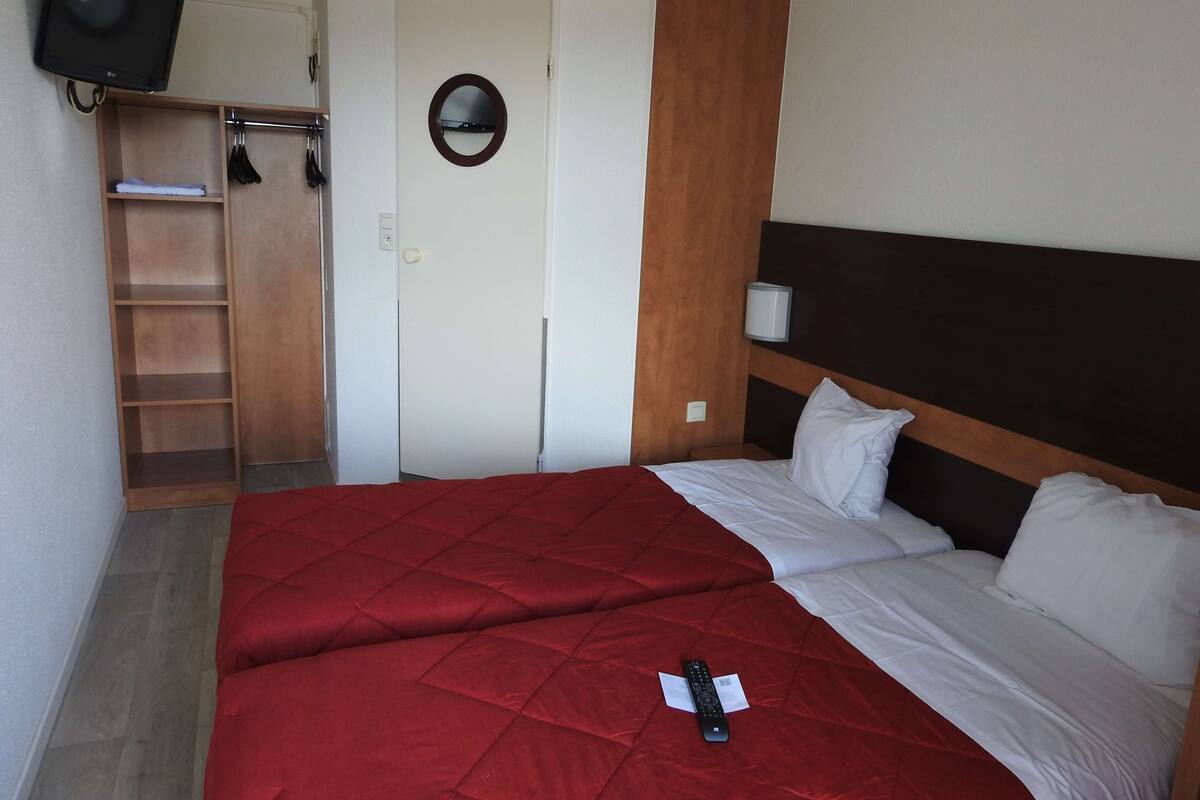 Habitación de hotel con una cama, un televisor montado en la pared, un armario de madera y una puerta con espejo.
